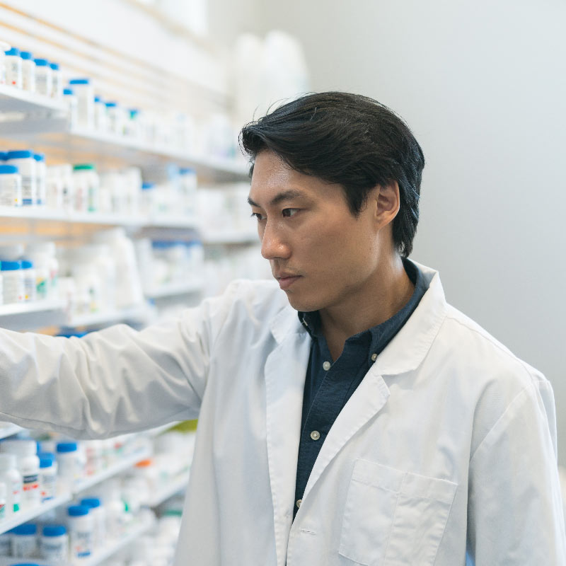 Young Asian female pharmacist in white labcoat stands confidently with arms crossed, in pharmacy